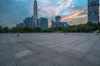 a city skyline is shown from the ground at sunset, and a person walks on the pavement