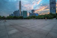 a city skyline is shown from the ground at sunset, and a person walks on the pavement