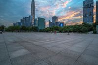 a city skyline is shown from the ground at sunset, and a person walks on the pavement