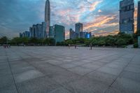 a city skyline is shown from the ground at sunset, and a person walks on the pavement