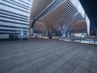 a walkway with some kind of roof on it at night in front of building with lights