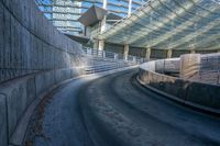 an empty street in front of a stadium with curved roof and concrete walls with stairs