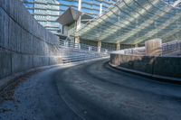 an empty street in front of a stadium with curved roof and concrete walls with stairs