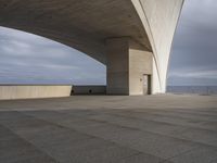 a large, concrete structure on the edge of a lake under an overcast sky