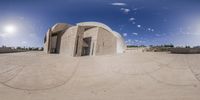 a spherical panoramic image of a large concrete structure on an island with blue sky above