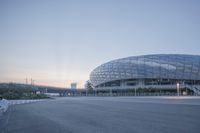 an arena is seen near a road with benches beside it at sunset in a city