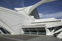 a person holding an umbrella walks towards an modern building with curved designs on the side