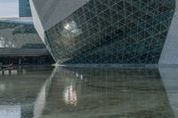 an image of a glass structure building with reflectioning water in the foreground and a person walking in the center