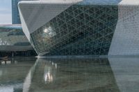 an image of a glass structure building with reflectioning water in the foreground and a person walking in the center