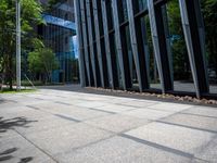 a bench is in front of a large glass building near trees and lawns on the sidewalk