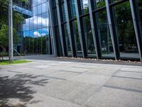 a bench is in front of a large glass building near trees and lawns on the sidewalk