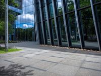 a bench is in front of a large glass building near trees and lawns on the sidewalk