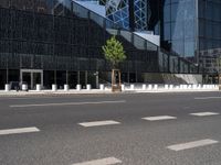 the empty road runs near the black and silver building with windows and a clock hanging on it