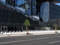 the empty road runs near the black and silver building with windows and a clock hanging on it