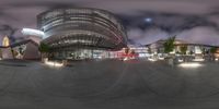 a very large building with buildings in the background at night time, as seen through an abstract 360 lens