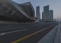 view of a big building with futuristic architecture by it's side and cars driving down the street