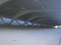 a person riding a skateboard down a sidewalk under a large structure of vaulted ceilings