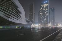 a large building sitting near a highway with skyscrapers in the background on a dark night