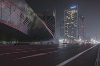 a large building sitting near a highway with skyscrapers in the background on a dark night