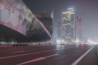 a large building sitting near a highway with skyscrapers in the background on a dark night