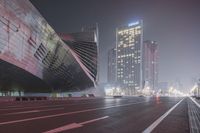 a large building sitting near a highway with skyscrapers in the background on a dark night