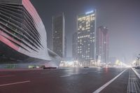 a large building sitting near a highway with skyscrapers in the background on a dark night