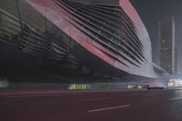 a large building sitting near a highway with skyscrapers in the background on a dark night