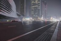 a large building sitting near a highway with skyscrapers in the background on a dark night