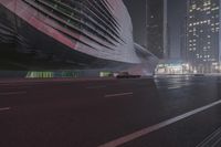 a large building sitting near a highway with skyscrapers in the background on a dark night