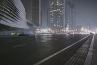 a large building sitting near a highway with skyscrapers in the background on a dark night