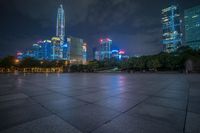 a city skyline lit up with many buildings in the background and a park with benches at its base