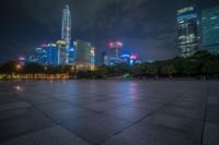 a city skyline lit up with many buildings in the background and a park with benches at its base