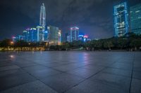 a city skyline lit up with many buildings in the background and a park with benches at its base