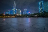 a city skyline lit up with many buildings in the background and a park with benches at its base