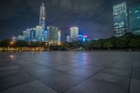 a city skyline lit up with many buildings in the background and a park with benches at its base