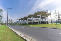 a large structure with multiple long columns on the side of a road next to grass and some buildings