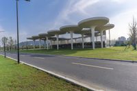 a large structure with multiple long columns on the side of a road next to grass and some buildings