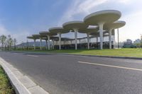 a large structure with multiple long columns on the side of a road next to grass and some buildings