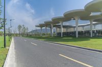 a large structure with multiple long columns on the side of a road next to grass and some buildings