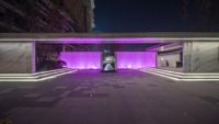 purple lighting illuminate a square shaped building at night, with sculptures sitting in front