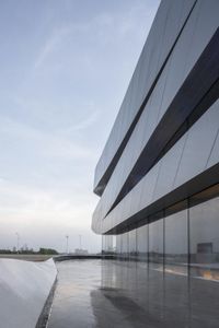 a modern structure made of thin white panels on an empty concrete floor overlooking a water surface