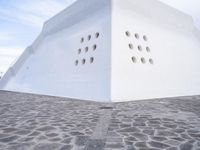 a white concrete structure with a large number of holes in the top of it and a blue sky overhead