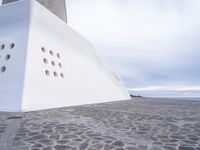 a white concrete structure with a large number of holes in the top of it and a blue sky overhead