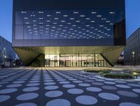 a building with lights and large holes on the concrete in front of it, lit up at night