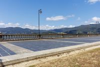 an empty parking lot on the side of a bridge with mountains in the background near a light post and street lamp