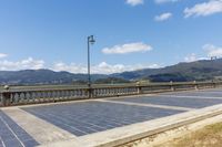 an empty parking lot on the side of a bridge with mountains in the background near a light post and street lamp