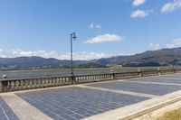 an empty parking lot on the side of a bridge with mountains in the background near a light post and street lamp