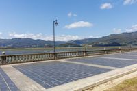 an empty parking lot on the side of a bridge with mountains in the background near a light post and street lamp