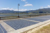 an empty parking lot on the side of a bridge with mountains in the background near a light post and street lamp