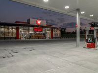 two gas pumps and a car wash station at dusk, with the awnings in bright light